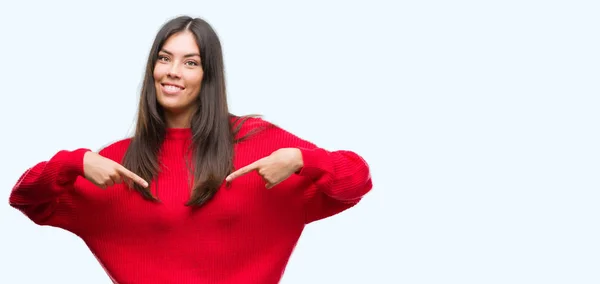 年轻漂亮的西班牙裔穿着红色毛衣看起来自信的脸上 指着自己的手指自豪和快乐 — 图库照片