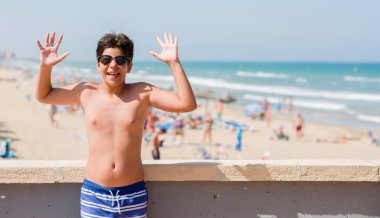 Kocaman bir gülümseme ile çığlık zaferini kutluyor ve ellerini kaldırdı beach çok mutlu ve heyecanlı, kazanan ifade, tatil günlerinde genç çocuk