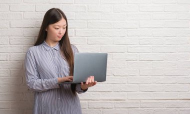 Acımak yüz ciddi düşünüyorum üstünde kendine güvenen bir ifade ile dizüstü kullanarak tuğla duvar üzerine Genç Çinli kadın