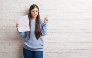 Genç Çinli kadın dilini beyaz tuğla duvarın üzerinden out komik ifade ile mutlu. Duygu kavramı.