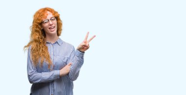 Mutlu yüz zafer işareti yaparken kameraya göz kırpıyor ile gülümseyen genç redhead bussines kadın. İki numaralı.