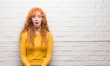 Tuğla duvar bir sürpriz yüz, korkuyor ve heyecanlı korku ifadesi ile şok korkmuş üzerinde duran genç Kızıl saçlı kadın