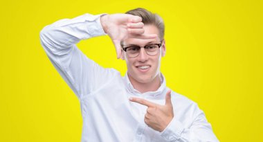 Elle yapma çerçeve ve parmakları ile mutlu yüz gülümseyen genç yakışıklı sarışın adam. Yaratıcılık ve Fotoğrafçılık kavramı.