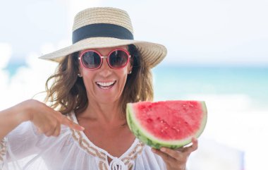 Orta yaş esmer kadın sürpriz yüz işaret parmağı kendine karpuz yeme deniz tarafından