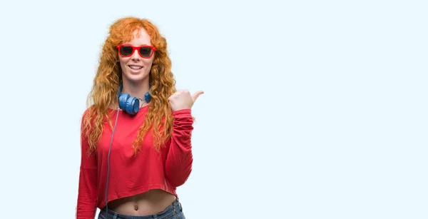 Mujer Pelirroja Joven Con Auriculares Apuntando Mostrando Con Pulgar Hacia —  Fotos de Stock