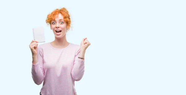 Giovane Rossa Donna Possesso Quaderno Bianco Urlando Orgoglioso Celebrando Vittoria — Foto Stock