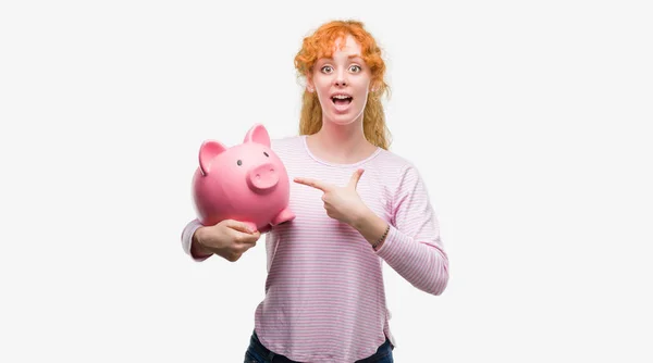 Junge Rothaarige Frau Hält Sparschwein Sehr Glücklich Zeigt Mit Hand — Stockfoto