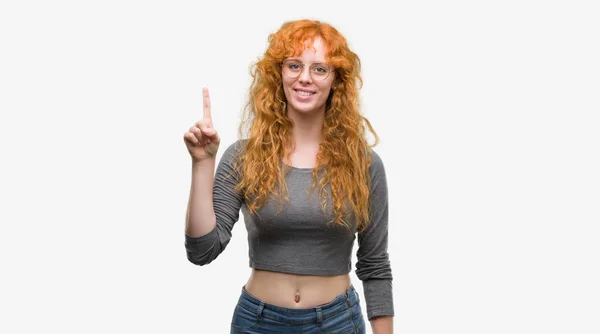 年轻的红头发的妇女显示和指着手指头号 而微笑的信心和快乐 — 图库照片