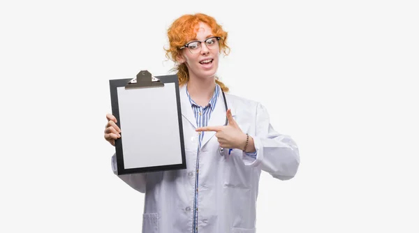 Joven Pelirroja Doctora Sosteniendo Portapapeles Muy Feliz Señalando Con Mano —  Fotos de Stock