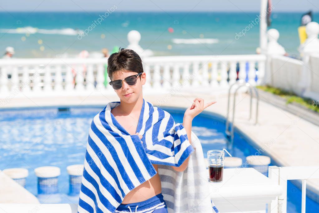 Young child on holiday at the swimming pool by the beach very happy pointing with hand and finger to the side