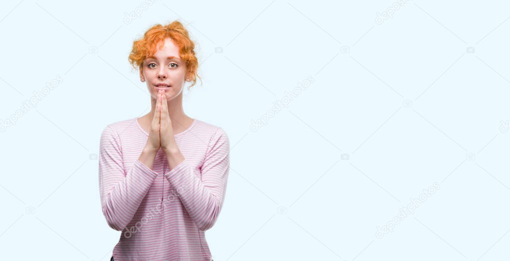 Young redhead woman praying with hands together asking for forgiveness smiling confident.