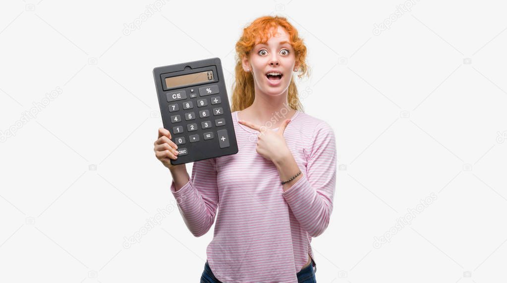 Young redhead woman holding big calculator very happy pointing with hand and finger