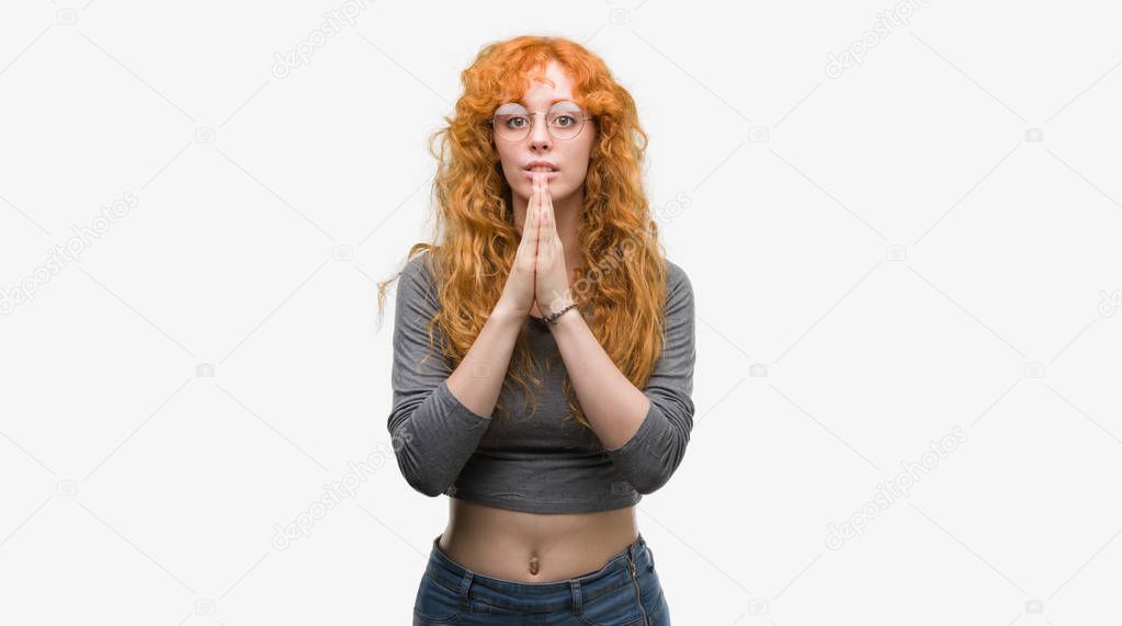 Young redhead woman praying with hands together asking for forgiveness smiling confident.