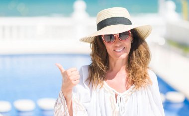 Orta yaş esmer kadın işaret ve başparmak kadar mutlu yüz gülümseyen tarafı ile gösterilen havuz kenarında