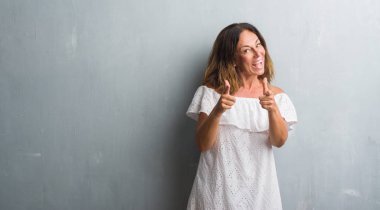 Fotoğraf makinesi ile mutlu ve komik yüz için parmakları işaret gri grunge duvarın üzerinden duran orta yaş İspanyol kadın. İyi enerji ve vibes.