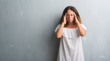 Orta yaş İspanyol kadın baş baş ağrısı için el ile gri grunge duvarın üzerinden çünkü ayakta stres. Migren muzdarip.