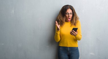 Orta yaş İspanyol kadın büyük gülümseme ile çığlık ve ellerini kaldırdı zaferini kutluyor smartphone çok mutlu ve heyecanlı, kazanan ifade kullanma