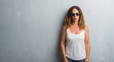 Orta yaş İspanyol kadın gri duvar yüzünde ciddi bir ifade ile güneş gözlüğü takıyor. Basit ve doğal kameraya bakıyor.