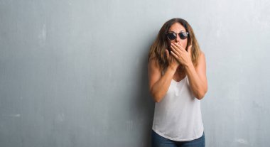 Orta yaş İspanyol kadın gri duvar eller için hata ile ağız kapsayan şok güneş gözlüğü takıyor. Gizli kavramı.