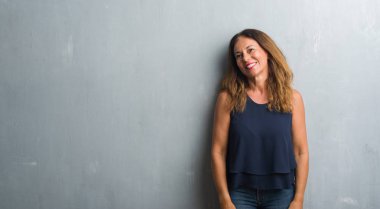 Gri grunge duvar uzak tarafına gülümseme ile yüzünde, doğal ifade seyir duran orta yaş İspanyol kadın. Kendine güvenen gülüyor.