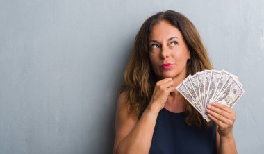 Orta yaş İspanyol kadın düşünmeye soru, çok karışık fikir ciddi bir yüz dolar tutan gri grunge duvarın üzerinden ayakta