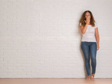 Beyaz tuğla duvar kapağı ağız elle hata, korku, ifade için utanç ile şok üzerinde duran orta yaş İspanyol kadın sessizce, gizli kavramı korkuttu