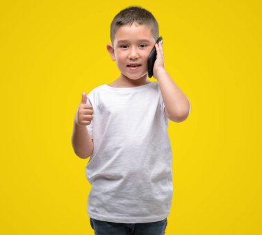 Koyu saçlı küçük çocuk ok işareti, başparmak ile parmak, mükemmel işareti yapıyor kocaman bir gülümseme ile mutlu bir smartphone kullanarak