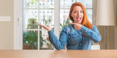 Kızıl saçlı kadın evde şaşırdım ve el ile sunulması ve parmak ile işaret ederken kameraya gülümseyen.