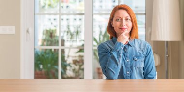 Kızıl saçlı kadın evde emin çapraz kollar ve çeneme kaldırdı el ile gülümseme ile kameraya bakıyor. Pozitif düşünce.