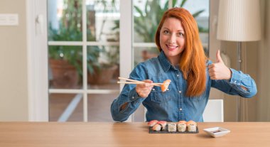 Ok işareti, başparmak ile parmak, mükemmel işareti yapıyor kocaman bir gülümseme ile mutlu yemek çubukları kullanarak suşi yemek Kızıl saçlı kadın