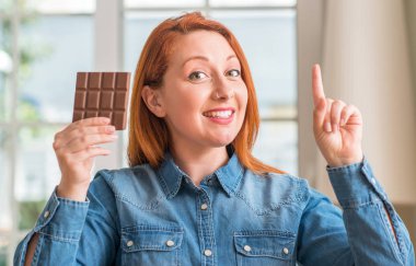 Çikolata bar evde bir fikir ya da soru işaret parmağı gülen yüz, bir numara ile sürpriz tutan Kızıl saçlı kadın