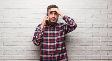 Kafasına, utanç ve sürpriz yüz ile şok el ile vurguladı beyaz tuğla duvarın üzerinden ayakta telefonda konuşan genç yetişkin adam öfkeli ve sinirli. Korku ve hata için üzgün.