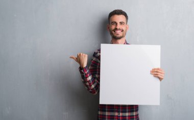 Genç yetişkin adam işaret ve başparmak kadar mutlu yüz gülümseyen tarafı ile gösterilen tuğla duvar holding afiş üzerinde