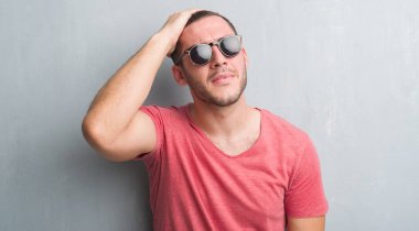 Genç beyaz adam baş, el ile vurguladı güneş gözlüğü takıyor gri grunge duvarın üzerinden şok utanç ve sürpriz suratla, öfkeli ve sinirli. Korku ve hata için üzgün.