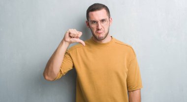 Kızgın yüz, eksi işareti aşağı antipati başparmak ile gösterilen, ret kavramı ile gri grunge duvarın üzerinden beyaz delikanlı