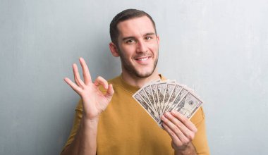 Parmak, mükemmel sembolü ile ok işareti yapıyor dolar tutan gri grunge duvarın üzerinden beyaz delikanlı