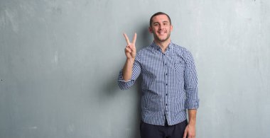 Beyaz delikanlı gösterilen ve parmakları ile işaret gri grunge duvarın üzerinden ikincisi ise kendinden emin ve mutlu gülümseyerek.