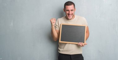 Duygu tezahürat Genç beyaz adam gurur çığlık ve zafer ve başarı çok heyecanlı, kutluyor blackboard tutan gri grunge duvarın üzerinden