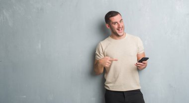 Gri grunge üzerinde beyaz delikanlı duvar manifatura smartphone el ve parmak ile işaret çok mutlu kullanarak bir ileti