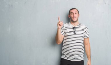 Gri grunge Genç beyaz adam başarılı fikirle işaret parmağı duvar. Çıktıktan ve mutlu. Bir numara.