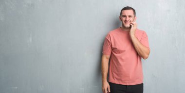 Beyaz delikanlı diş ağrısı veya dişlerde dişlerle ilgili hastalık nedeniyle ağız acı ifadesi ile el ile dokunmak gri grunge duvarın üzerinden. Diş hekimi kavramı.