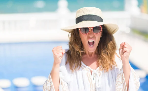 Middle age brunette woman by the swiming pool annoyed and frustrated shouting with anger, crazy and yelling with raised hand, anger concept