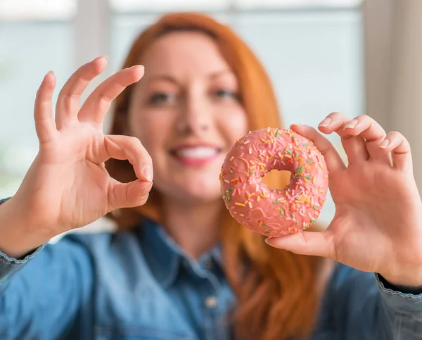 Pelirroja Mujer Sosteniendo Donut Casa Haciendo Signo Con Los Dedos —  Fotos de Stock