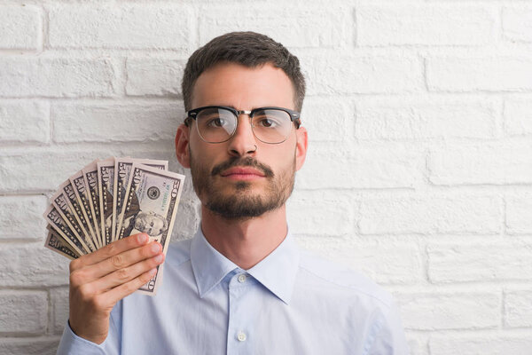 Young hipster business man holding dollars with a confident expression on smart face thinking serious