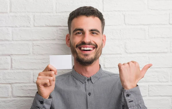 Ung Vuxen Man Över Tegelvägg Håller Tomt Kort Pekar Och — Stockfoto