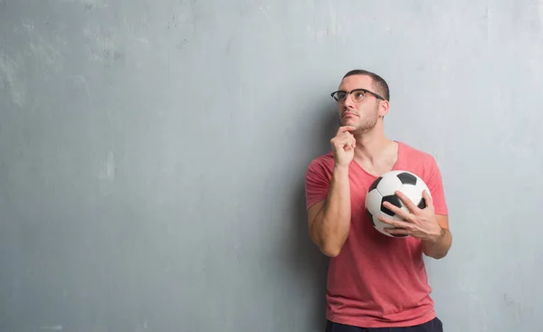 Jovem Caucasiano Sobre Parede Grunge Cinza Segurando Bola Futebol Rosto — Fotografia de Stock