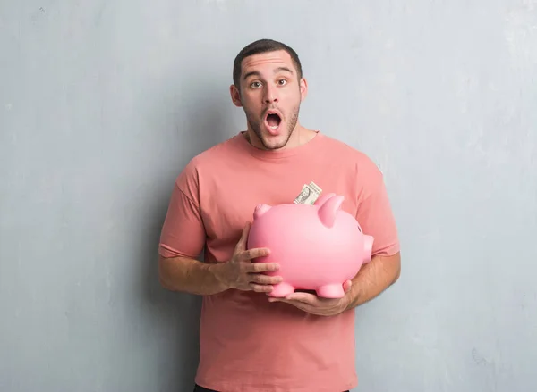 Young Caucasian Man Grey Grunge Wall Holding Piggy Bank Scared — Stock Photo, Image