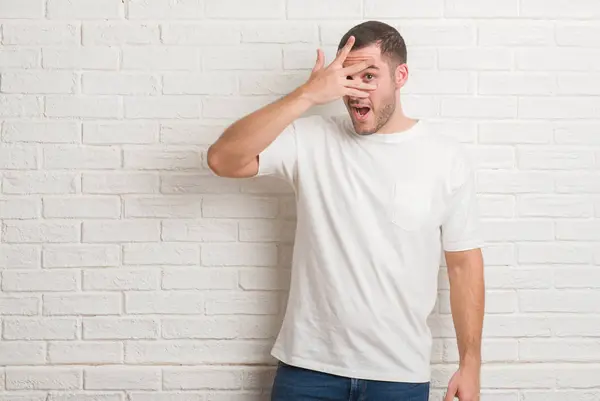 Jovem Caucasiano Sobre Parede Tijolo Branco Espreitando Choque Cobrindo Rosto — Fotografia de Stock