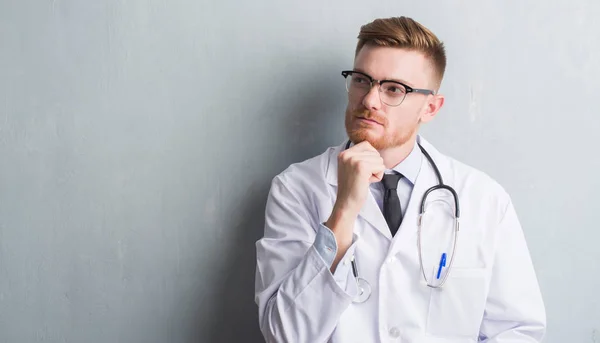 Young Redhead Doctor Man Grey Grunge Wall Serious Face Thinking — Stock Photo, Image