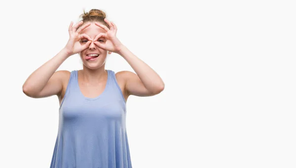 若いブロンドの女性は舌を出して指を通して見る目をこだわりの双眼鏡のような のジェスチャーを行います クレイジー式 — ストック写真